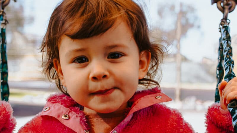 Close up of young child on a swing outside smirking at the camera