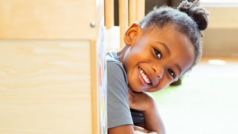 Young child in a classroom setting siting and smiling at the camera
