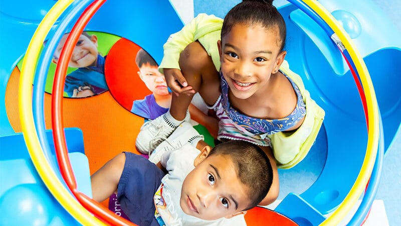 Two students behind a very colorful background looking up at the camera